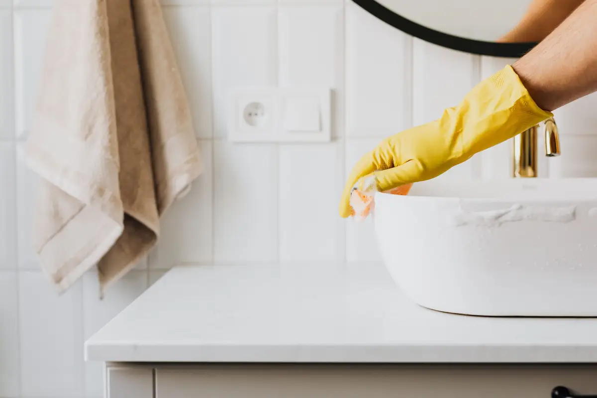 Gloved hand cleaning a white bathroom sink
